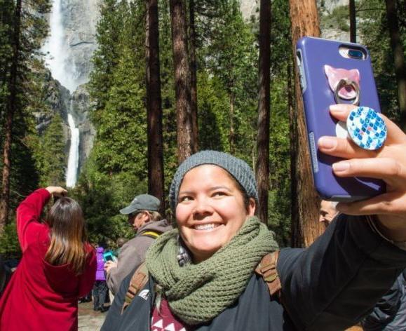 a student takes a selfie at a national park with a waterfall in the background